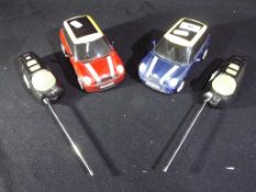 Two Mini Cooper remote control cars with remote controls and aerials.