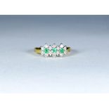 A three stone emerald ring surrounded by diamonds, set in 18ct yellow gold, ring size Q,