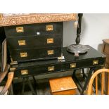 A black military style desk with brass handles and a similar chest of four drawers