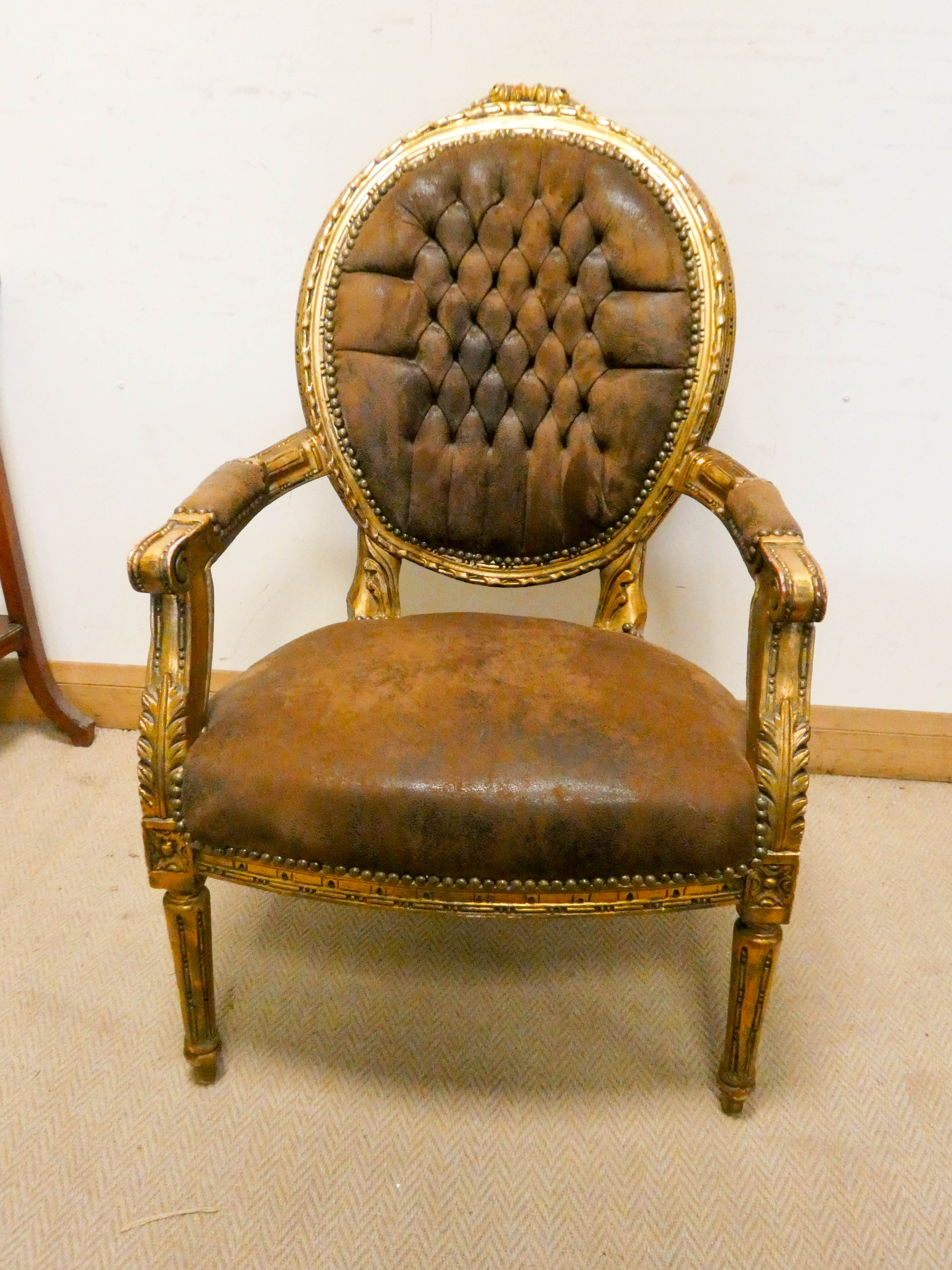 A French gilt framed elbow chair with brown leather upholstered seat and buttoned leather back