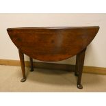 A Georgian circular oak drop leaf dining table standing on pad feet,