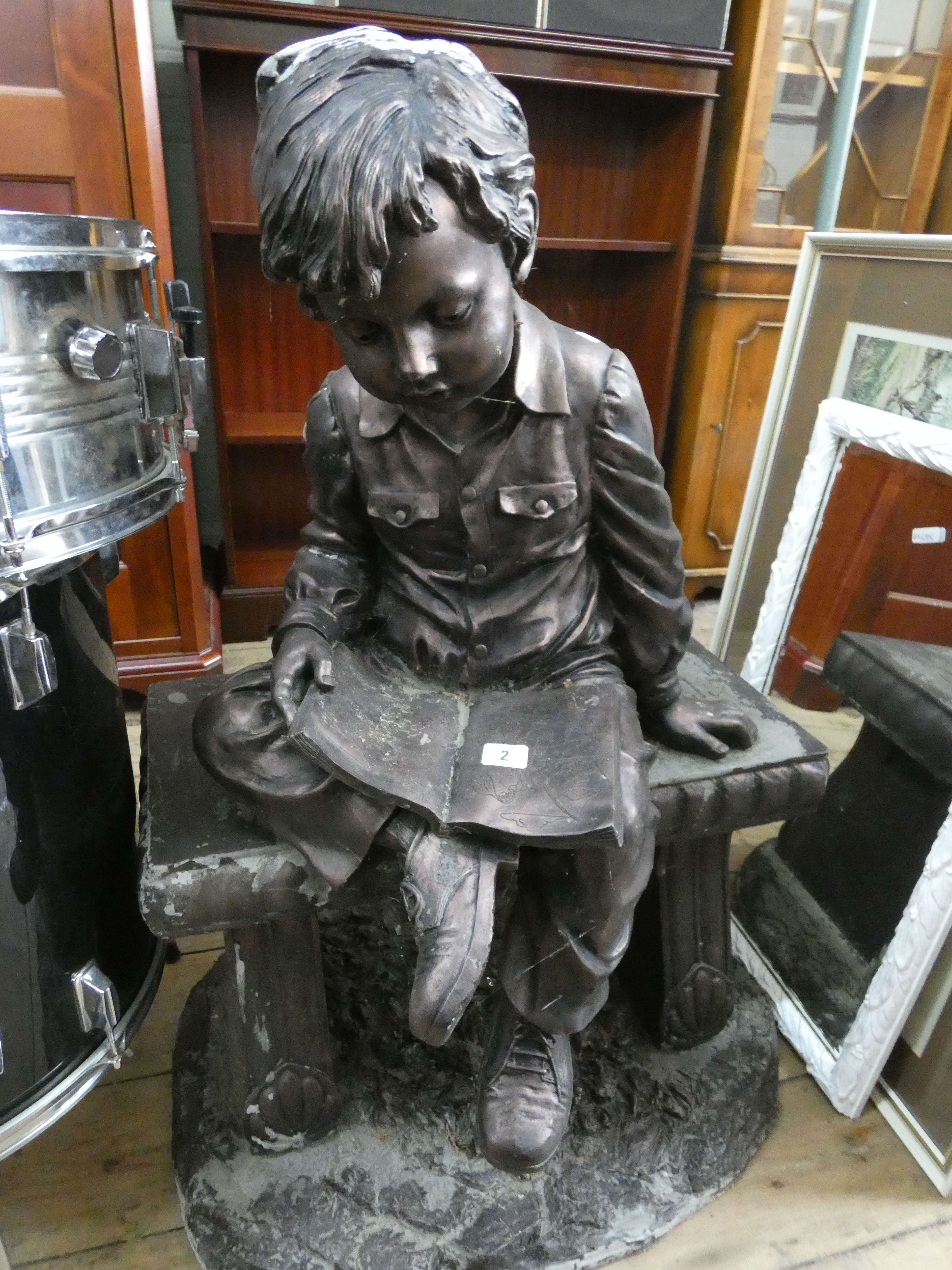 A resin garden ornament of a young boy reading a book on a bench