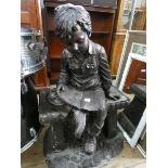 A resin garden ornament of a young boy reading a book on a bench