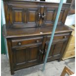 A reproduction Ercol oak court cupboard with a sliding cupboard back,