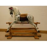 A small dapple grey rocking horse with saddle on wooden base