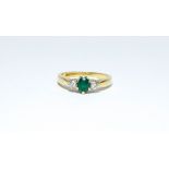 An 18ct three stone ring with a central oval emerald flanked by two modern brilliant cut diamonds,