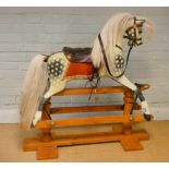 A small dapple grey rocking horse with leather saddle standing on wooden base