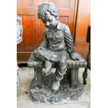 A resin garden ornament of a young boy reading a book on a bench