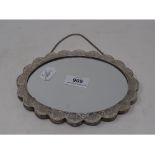 An Indian silver coloured metal mounted mirror, of shaped oval form, embossed flowers and foliage,