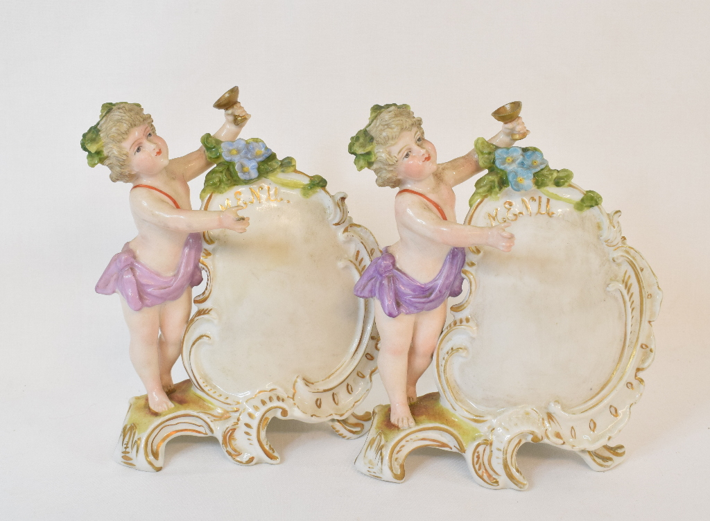 Two German porcelain menu holders, applied putto, 14 cm high, Continental, nodding and other figures