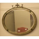 An oval mirror, the silvered frame surmounted an urn and swag decoration, 67 cm wide