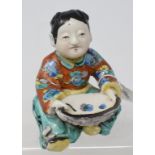 A Chinese porcelain figure, in the form of a seated boy, with polychrome decoration, 11 cm high