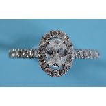 An 18ct white gold and diamond ring, the central oval cut stone within a diamond halo on diamond set