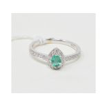 An 18ct white gold, pear shaped emerald and diamond cluster ring, with diamond set shoulders,