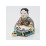 A Chinese porcelain figure, in the form of a seated boy, with polychrome decoration, 11 cm high