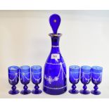 A blue glass liqueur set, with white enamel and gilt decoration, the decanter and stopper 33.5 cm