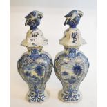 A pair of Dutch Delft vases, the covers with bird finials, the bases decorated dwellings, 34 cm high