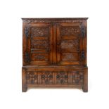 An oak cupboard on stand, carved flowers and foliage, having a pair of panel doors, the base with