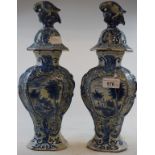 A pair of Dutch Delft vases, the covers with bird finials, the bases decorated dwellings, 34 cm high
