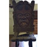A pair of African carved hardwood chairs, the backs worked as tribal masks, with hide seats (2)
