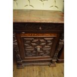 A carved oak cupboard, decorated masks and figures, with a single frieze drawer, 92 cm wide