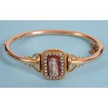 A late 19th century bangle, inset a carved hardstone cameo, within a surround of seed pearls See