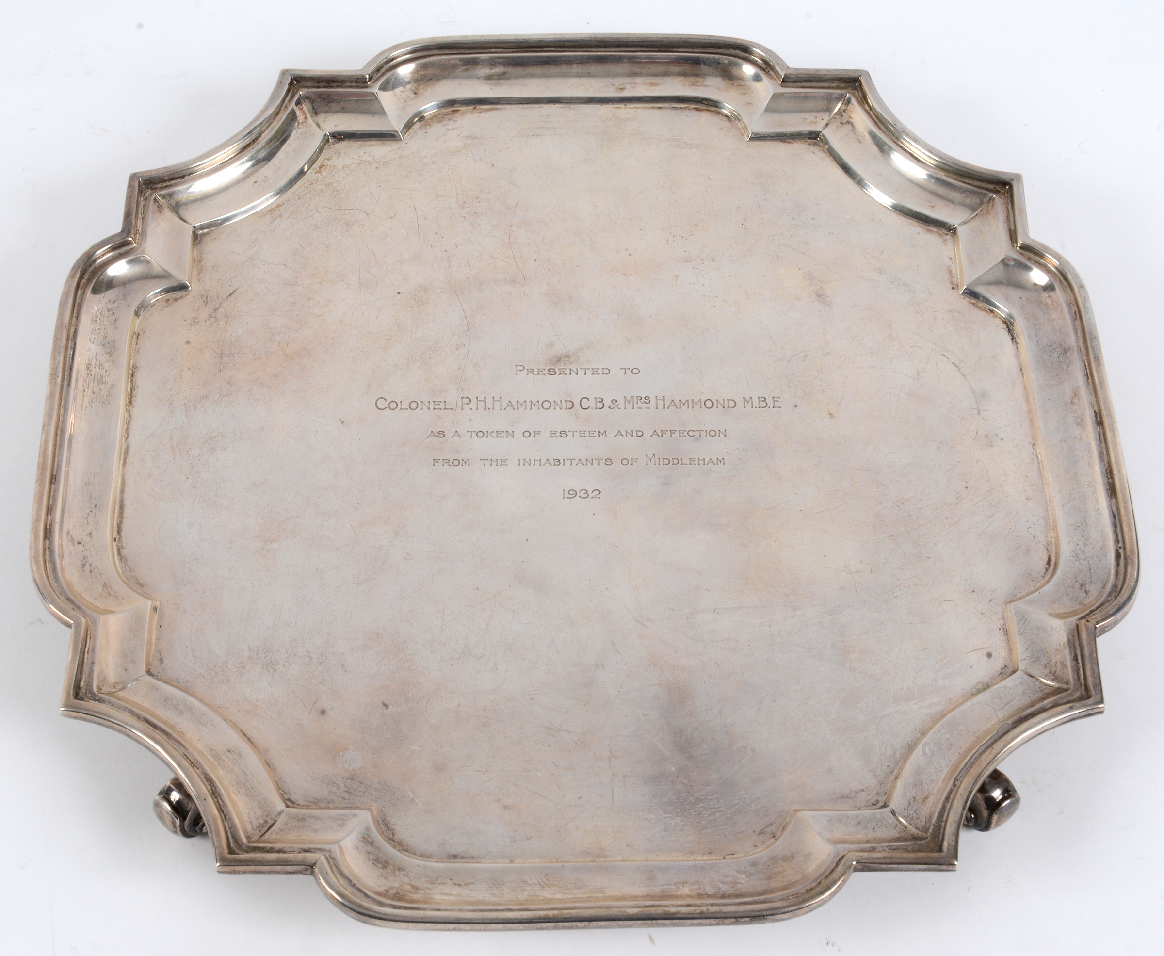 A silver salver, of shaped square form, with presentation inscription and dated 1932, on four scroll