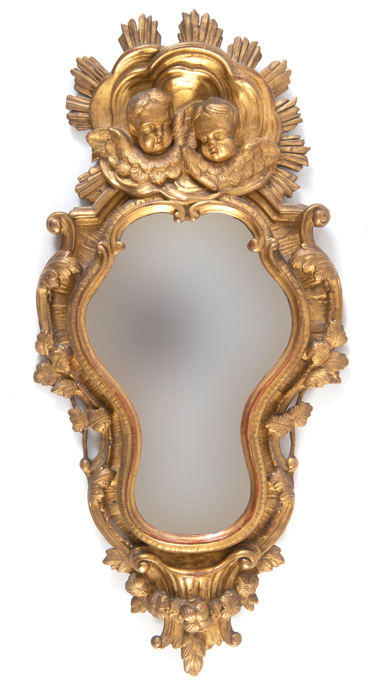 A Continental carved giltwood mirror, of shaped cartouche form, surmounted by cherub face masks,