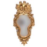 A Continental carved giltwood mirror, of shaped cartouche form, surmounted by cherub face masks,