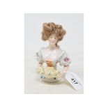 A porcelain half doll, lady with brown wig and floral dress, holding a basket of flowers, 13 cm high