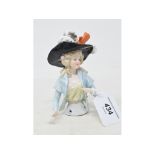 A porcelain half doll, lady wearing a large black hat and a light blue jacket, holding a card, 12 cm