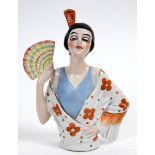 A porcelain half doll, Spanish lady with black hair, an orange comb and holding a fan, 15 cm high