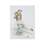 A porcelain half doll, lady wearing a yellow plumed hat and a green and white dress, holding posies,