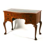 A walnut writing desk, the top with inset green leather above an arrangement of five drawers, on