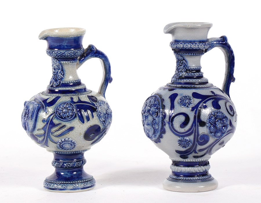 A near pair of continental stoneware jugs decorated with flowers and foliate scrolls in a crest, the