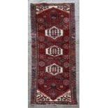 A Persian woollen runner with three central medallions within a stylised border on a red ground.