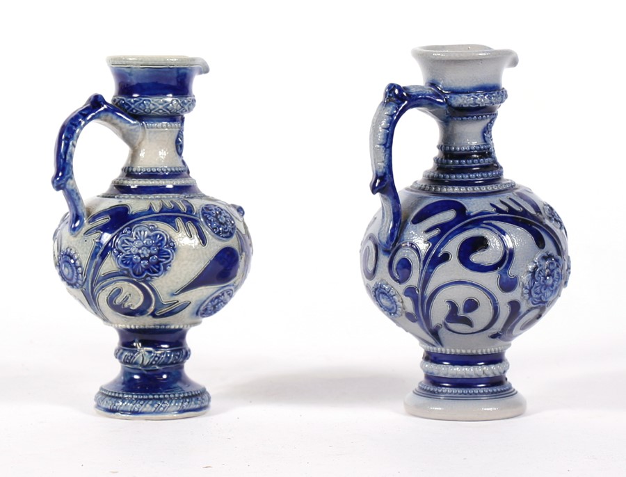 A near pair of continental stoneware jugs decorated with flowers and foliate scrolls in a crest, the - Image 2 of 2