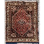 A Persian rug with central medallion within a stylised foliate border on a red ground, 103 by 153cms