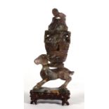 A Chinese purple figured hardstone figure depicting a deer carrying a lidded vase on its back,