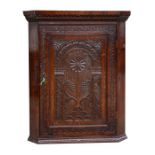 A 19th century oak corner cupboard, the panelled door carved with a central flower & fruit, 80cms (