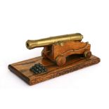A desk top brass and wood model of an 18th century Royal Navy 24 pounder cannon on a separate wooden