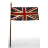 An early 20th century printed cotton Union Jack flag on its pole with a red finial. The flag is