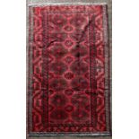 A Persian Balouch woollen handmade rug with repeat medallions on a red ground, 300 by 150cms (118 by