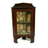 An Edwardian mahogany corner cupboard, the astragal glazed door enclosing a shelved interior,