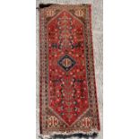 A Persian rug with central medallion and stylised flowers, on a red ground, 58.5 by 145cms (23 by