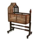 A Victorian mahogany swinging bassinet with bergere caned sides and Gothic form hood, on a turned