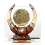 A Victorian brass dinner gong with cow horn supports on an oak base, 33cms (13ins) high.