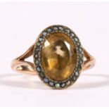 An Edwardian yellow metal ring set with a large oval pale yellow stone surrounded by seed pearls,