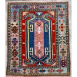 A handmade woollen Kazak rug decorated with geometric designs on a red ground, 194 by 279cms (76.5