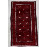 A Persian Baluch woollen handmade runner with three central guls within a stylised border on a red